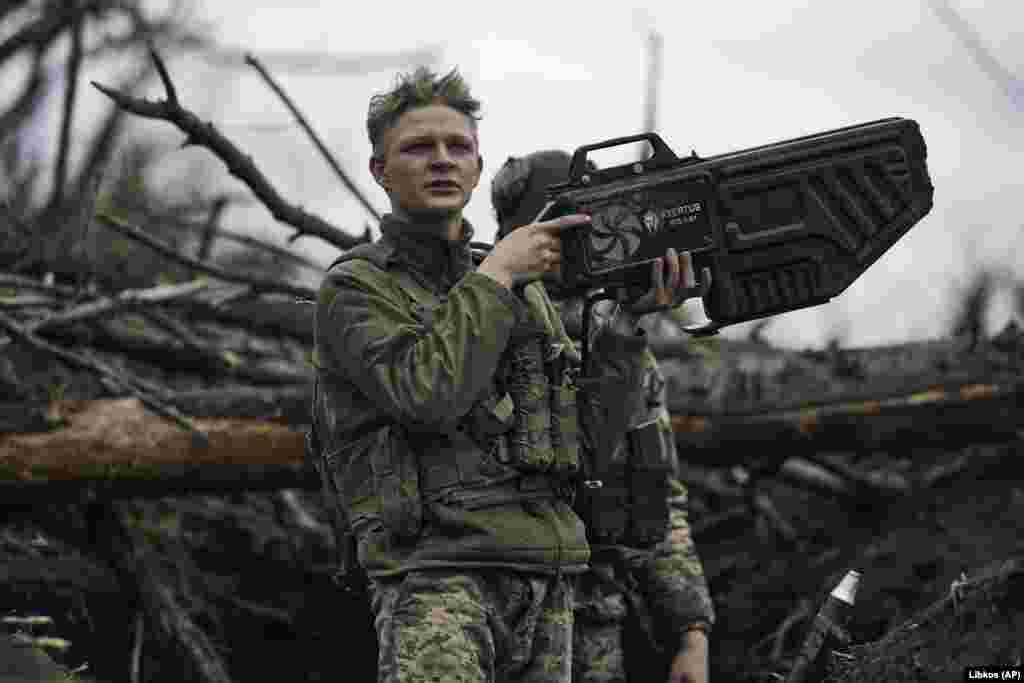 Un soldat ucrainean mânuiește o armă antidronă pe prima linie a frontului, lângă Avdiivka, în aprilie 2023. Dispozitivul de fabricație ucraineană, care costă 11 300 de dolari, utilizează unde radio direcționate pentru a perturba conexiunea dintre o dronă și operatorul acesteia. Interferențele pot întrerupe transmisiunea video și, în funcție de modelul dronei, o pot forța fie să se întoarcă la punctul de decolare, fie să aterizeze imediat, fie să intre în derivă purtată de vânt și eventual să se prăbușească.&nbsp;