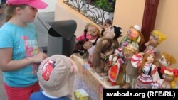 На сьвяточным кірмашы дзеці разглядаюць лялькі ў фальклёрных строях, падпісаныя «беларуска»